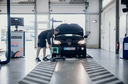 Ein Mechaniker arbeitet an einem schwarzen Volkswagen mit offenem Motorhaube in einer Werkstatt.