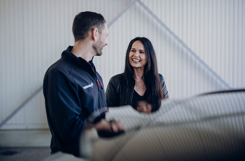 Ein Mann und eine Frau unterhalten sich in einer Werkstatt, beide lächeln.