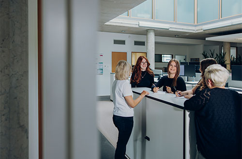 Gruppe von fünf Personen, die am Empfangstresen in einem modernen Büro stehen und miteinander sprechen.