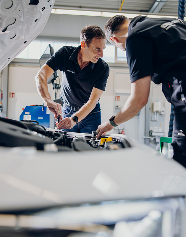Zwei Mechaniker arbeiten gemeinsam an einem Fahrzeugmotor in einer Werkstatt.