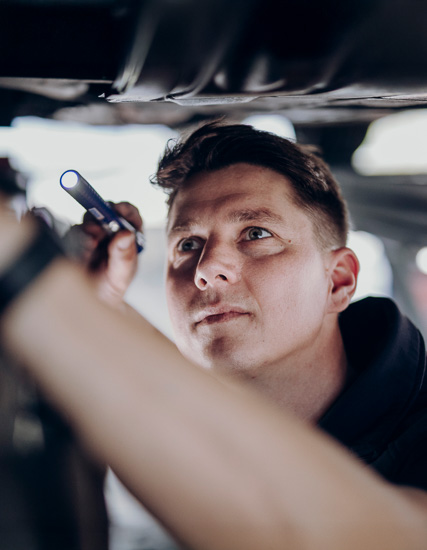 Mechaniker, der mit einer Taschenlampe unter einem Fahrzeug arbeitet und eine Inspektion durchführt.