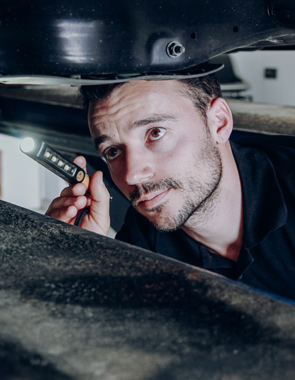 Mann mit Taschenlampe, der unter einem Fahrzeug nach technischen Details sucht.