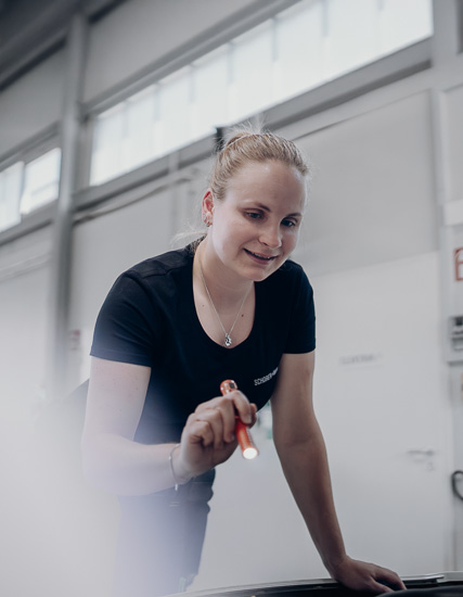 Frau mit einem Stift, die an einem Tisch in einem modernen Raum arbeitet und konzentriert aussieht.