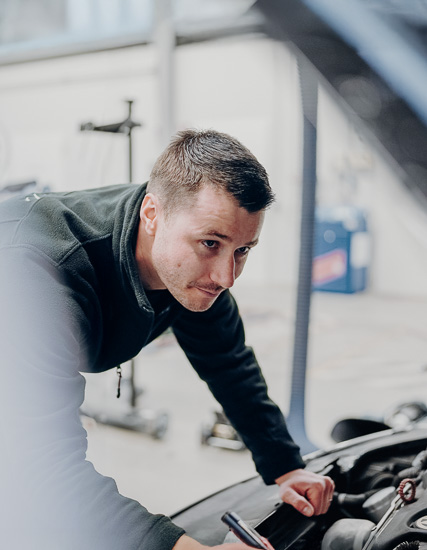 Mann, der an einem Auto arbeitet und den Motor inspiziert, während er sich konzentriert auf die Aufgabe fokussiert.