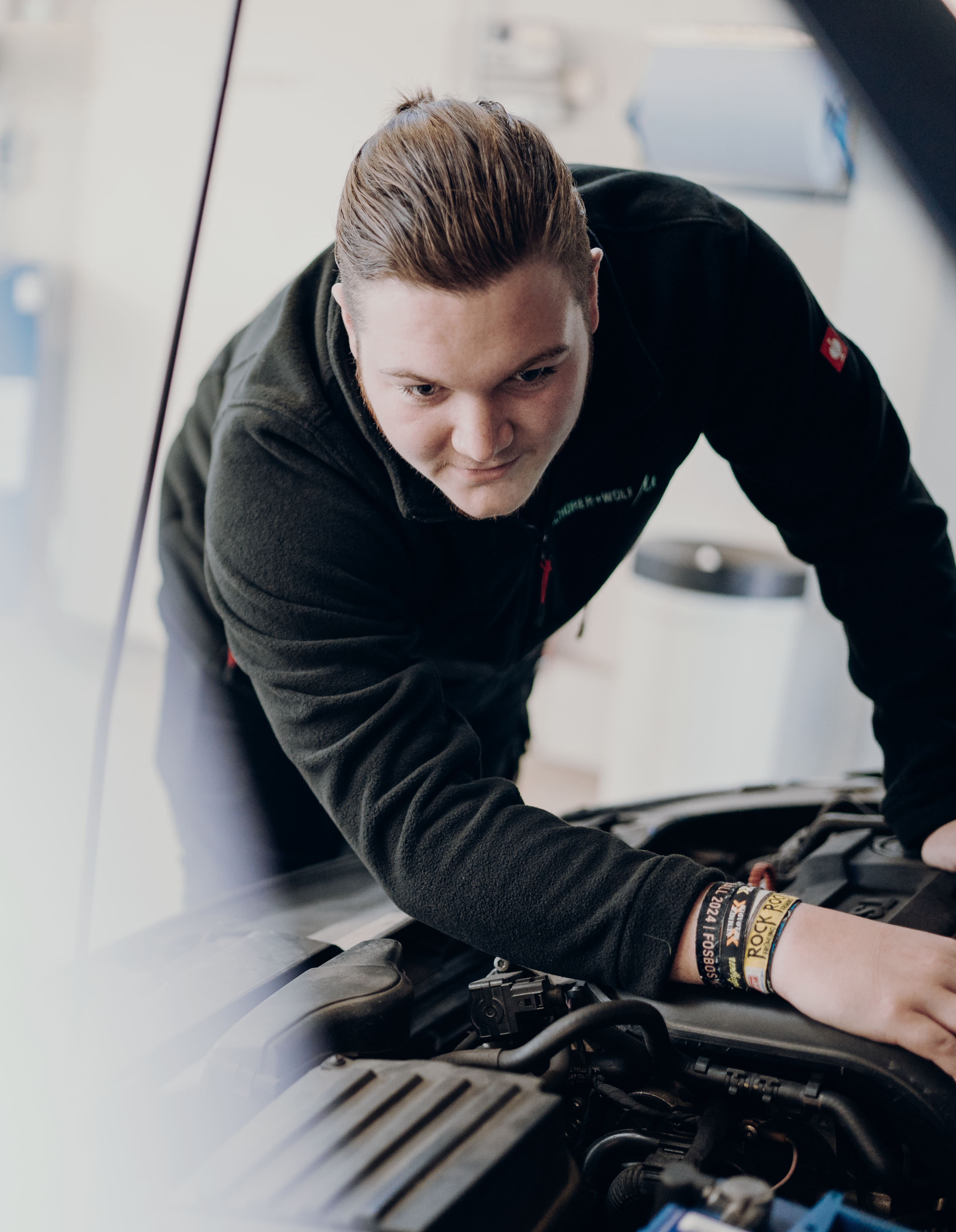 Jonas_427x550 Junger Mechaniker, der an einem Auto unter der Motorhaube arbeitet, mit einem konzentrierten Gesichtsausdruck.