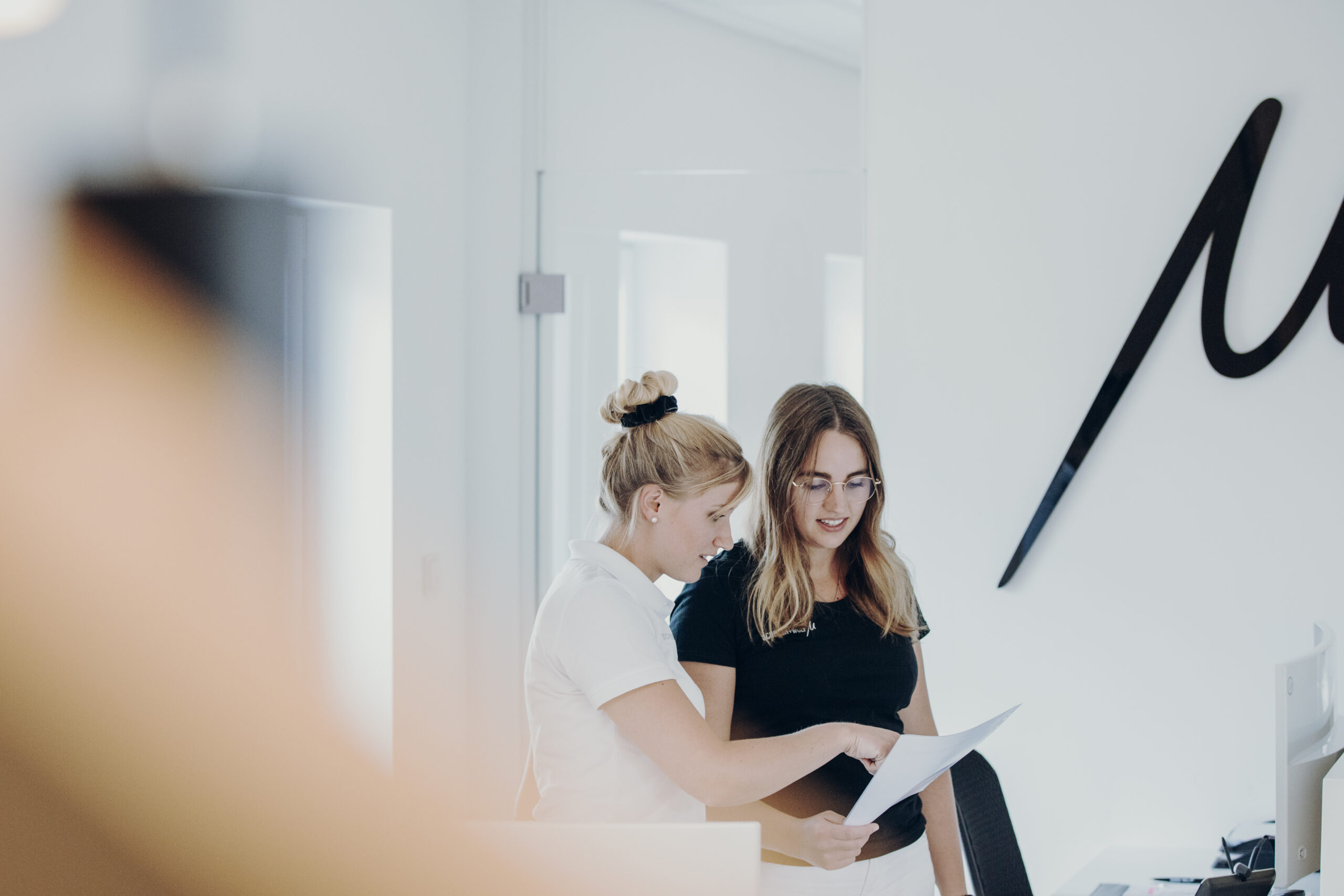 Zwei Frauen, eine mit blonden Haaren und eine mit braunen Haaren, betrachten ein Dokument in einem modernen Büro.